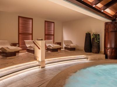 Luxuriöser Wellnessbereich mit Whirlpool, Holzliegen und indirekter Beleuchtung unter Holzdecke.