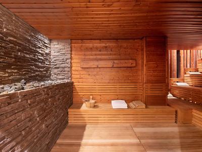 Gemütliche Sauna mit Holzwänden, Bänken, Handtüchern und Steinverkleidung an der linken Wand.
