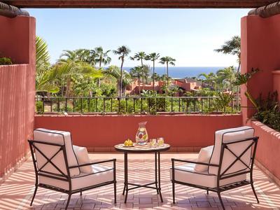 Terrasse mit zwei Sesseln, kleinem Tisch, Palmen und Blick auf das Meer im Hintergrund.