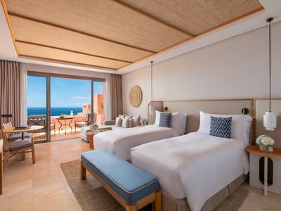 Helles Hotelzimmer mit zwei Betten, Balkon und Meerblick, modern eingerichteter Innenraum.