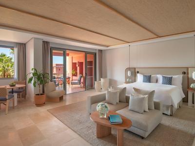 Helles, modernes Schlafzimmer mit großem Bett, Sessel, Kaffeetischen und Terrasse mit Pflanzen.