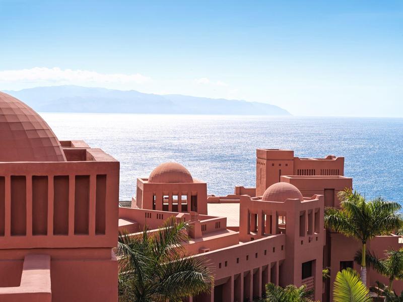Roze gebouwen met koepels en palmbomen aan zee onder een heldere lucht.