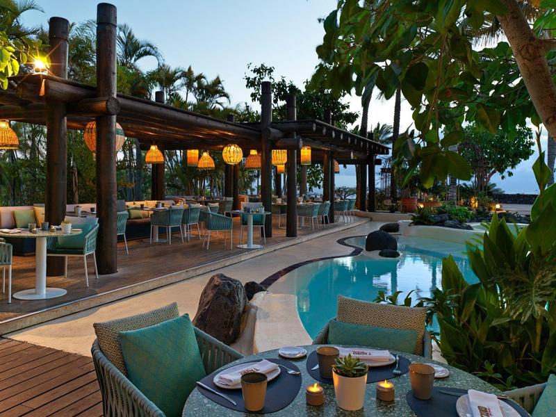 Avondterras met gezellige zitgedeeltes en een verlicht zwembad in een tropische omgeving.