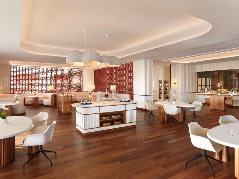 Licht, modern hotelrestaurant met houten vloeren, ronde tafels en stijlvolle witte stoelen.