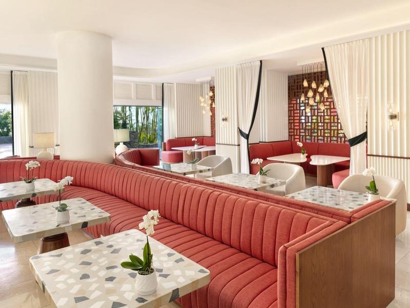 Helder modern hotelrestaurant met rode zitbanken en marmeren tafels naast een grote zuil.