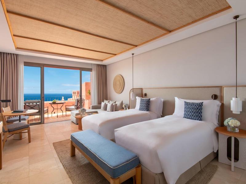 Modern hotelkamer met twee eenpersoonsbedden en zeezicht vanaf het balkon.