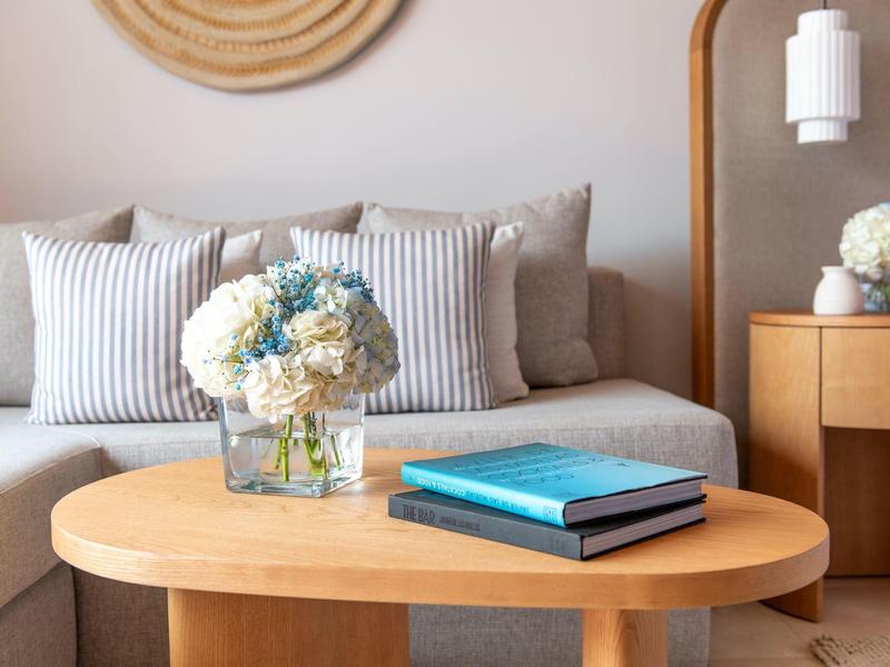 Gezellige woonkamer met houten salontafel, bloemenarrangement en kussens op de bank.