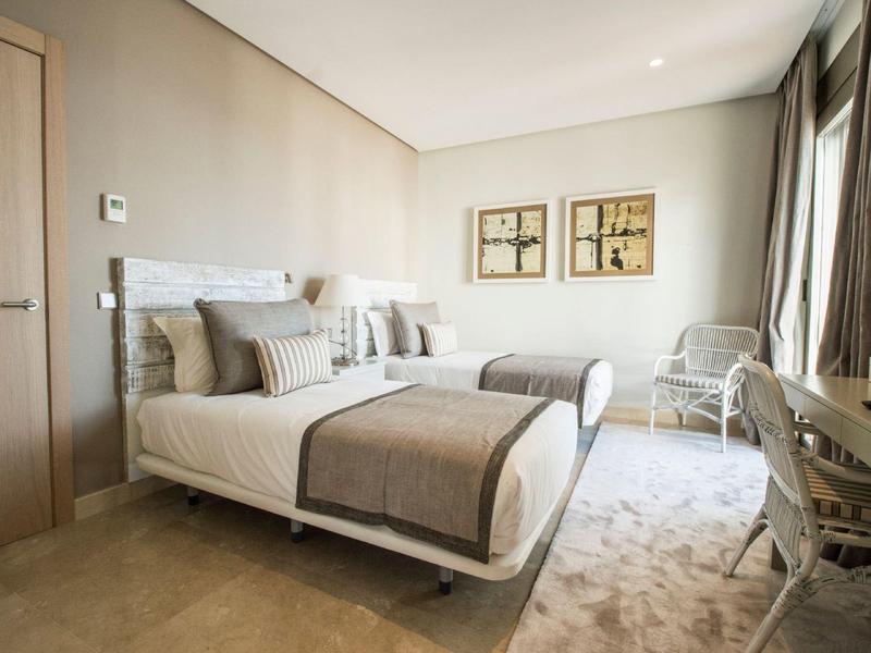 Chambre d'hôtel moderne avec deux lits simples, tons neutres et grandes fenêtres.