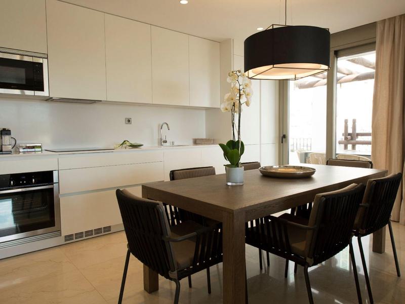 Cuisine moderne et salle à manger avec des armoires blanches et une table en bois avec des chaises noires.