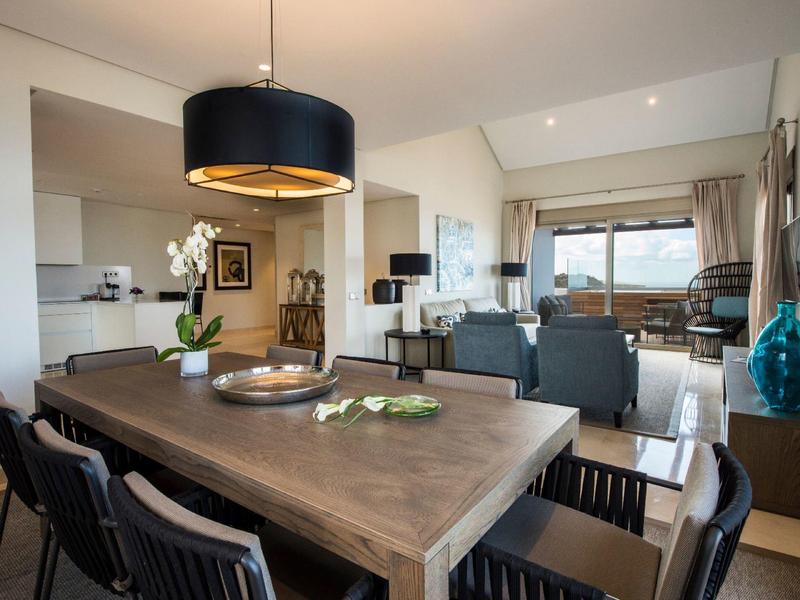 Espace salle à manger et salon moderne et ouverte avec grande table en bois et meubles de lounge près de grandes fenêtres.