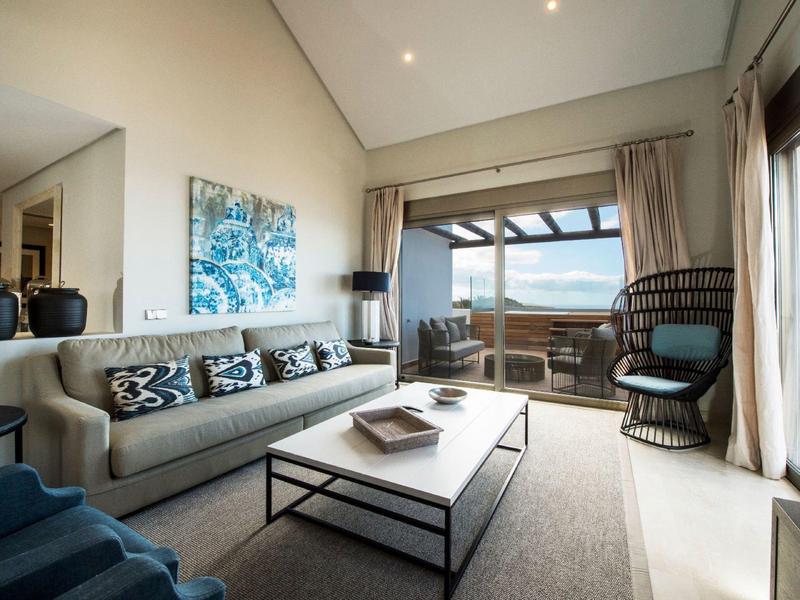 Salon moderne avec canapé, table et vue sur la mer à travers de grandes fenêtres.