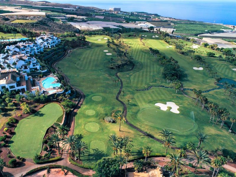 Terrain de golf vert avec bunkers de sable et hôtel adjacent près de la côte.
