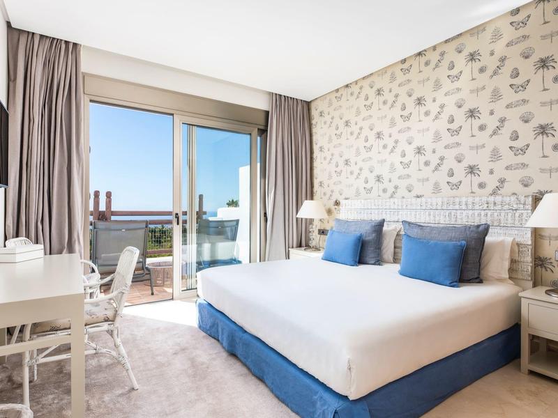 Chambre d'hôtel moderne avec grand lit double, bureau et balcon avec vue sur la mer.