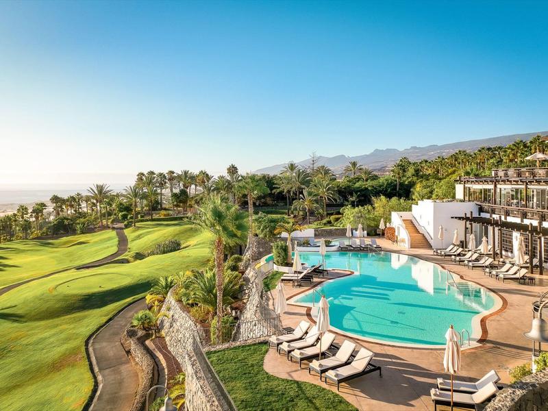Piscine d'hôtel avec transats à côté d'un parcours de golf verdoyant et de palmiers sous un ciel clair.