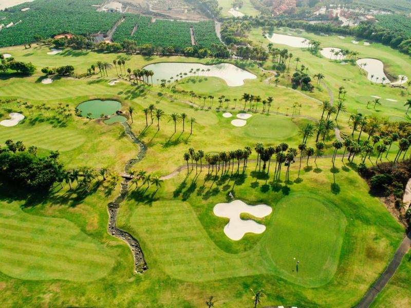 Vue aérienne d'un vaste parcours de golf avec des bunkers et des obstacles d'eau dans un paysage verdoyant.