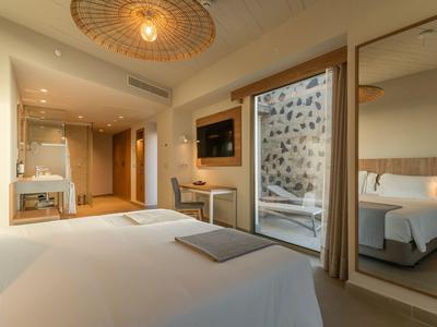 Modern hotel room with large bed, glass-walled bathroom, and warm lighting.