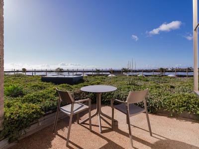 Table and two chairs on balcony overlooking green garden and blue sky.
