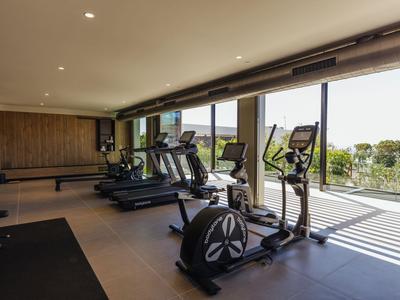 Moderner Fitnessraum mit verschiedenen Trainingsgeräten und großen Fenstern mit Außenaussicht.