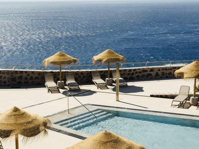 Pool area with sun loungers and thatched umbrellas overlooking the sea.