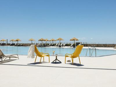 Zone de piscine vide avec des chaises jaunes et des parasols sous un ciel bleu.