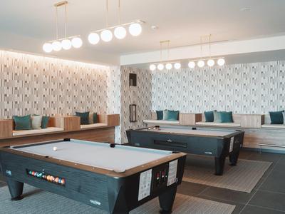 Modern game room with two pool tables and bench seating with cushions.