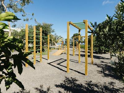 Outdoor-Spielplatz mit Klettergeräten und grünen Büschen unter blauem Himmel.