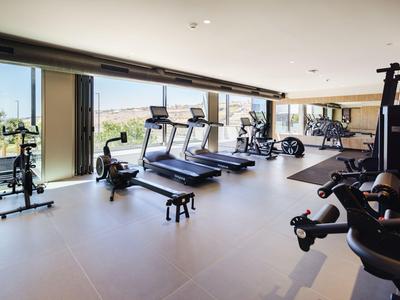 Moderner Fitnessraum mit Laufbändern, Fahrrädern und Kraftgeräten in hellem Raum mit Fensterblick