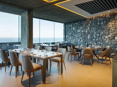 Modern restaurant with panoramic windows and sea view, table groups with chairs.