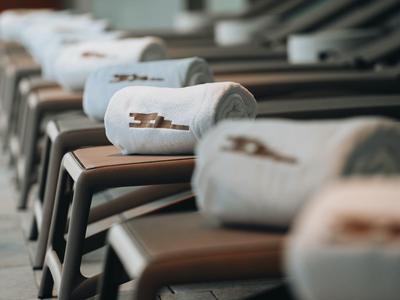 Row of lounge chairs with white rolled towels by the pool.