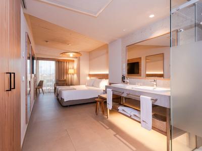 Modern hotel room with double bed, desk, large mirror, and semi-open bathroom.
