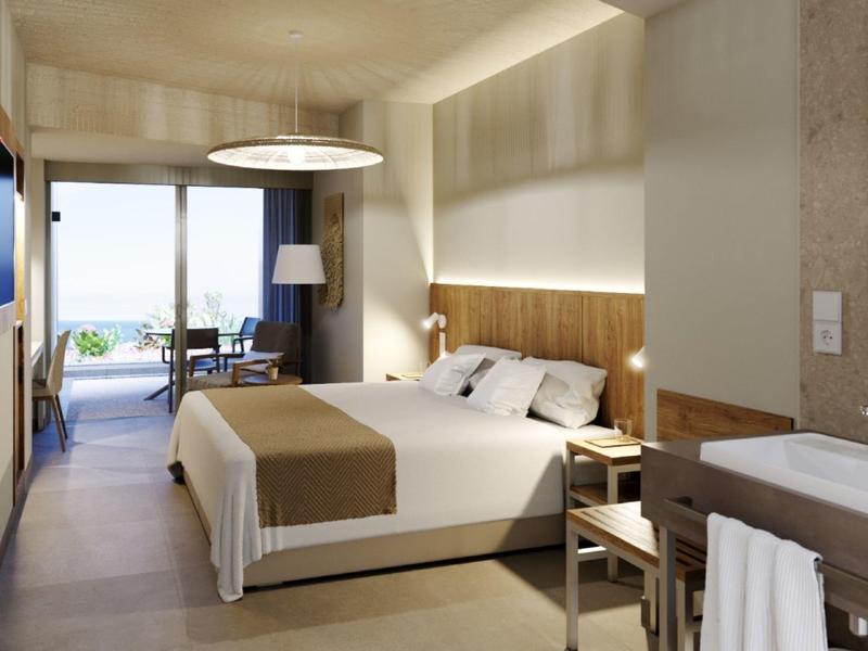 Modern hotel room with double bed, large windows, and view of terrace overlooking the sea.