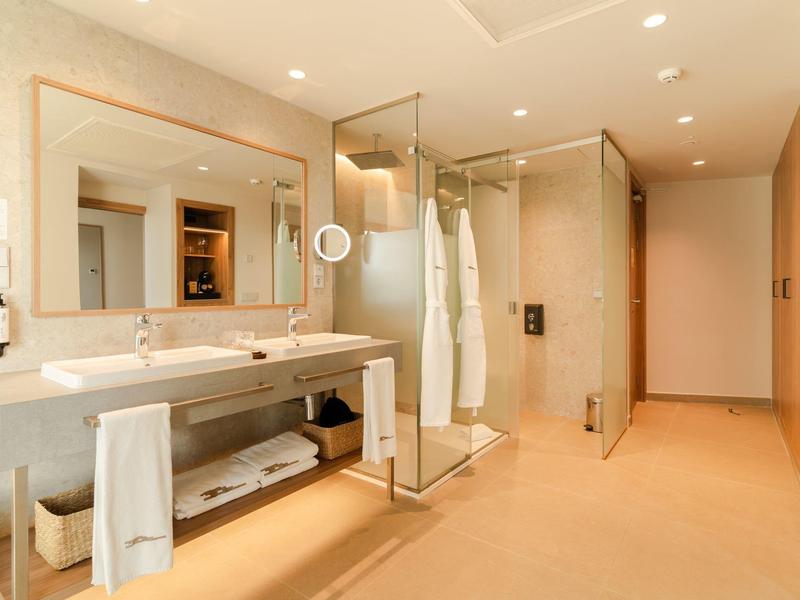 Modern bathroom with double sinks, large shower, and beige tiles.