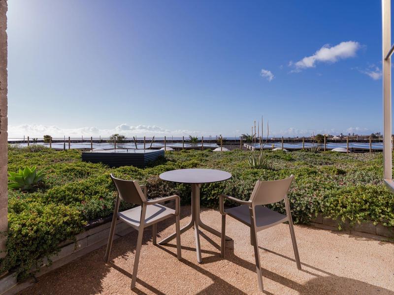 Table and two chairs on balcony overlooking green garden and blue sky.