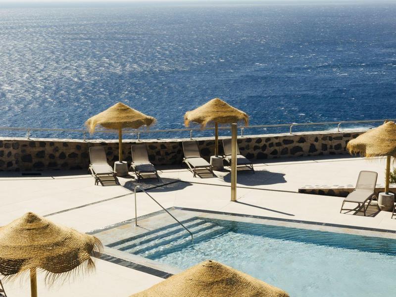 Pool area with sun loungers and thatched umbrellas overlooking the sea.