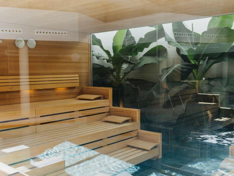 Interior of a wooden sauna with a view of a pool and greenery.