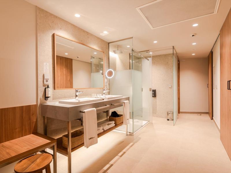 Modern hotel bathroom with large shower, double sinks, and wood accents.