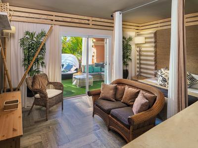 Acogedor área de estar con sofá de cuero y silla junto a grandes ventanas en una habitación de hotel.