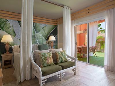 Acogedora zona de estar con cojines verdes junto a ventanas de techo a suelo, vista al balcón y jardín.