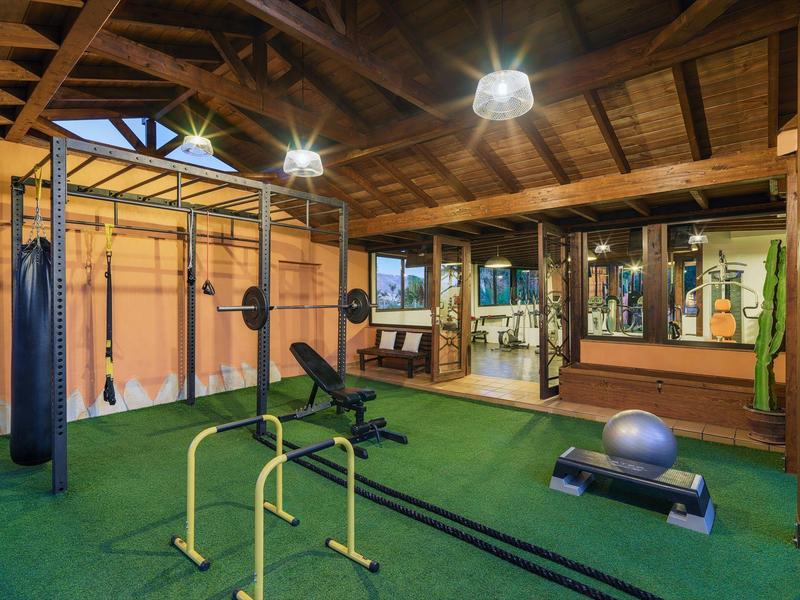 Helle Trainingshalle mit Holzdecke, grüner Gummimatte und vielseitigen Fitnessgeräten.