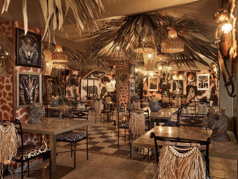 Rustikales Interieur mit Holztischen, Stühlen, Pflanzen und vielseitiger Dekoration in warmem Licht.