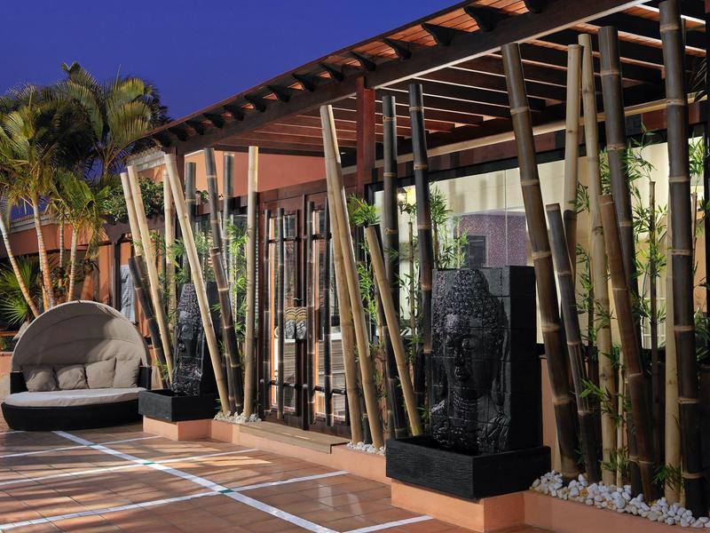 Moderner Außenbereich mit Bambuspflanzen, Buddha-Skulptur, runden Lounge-Sessel und Holzterrasse.