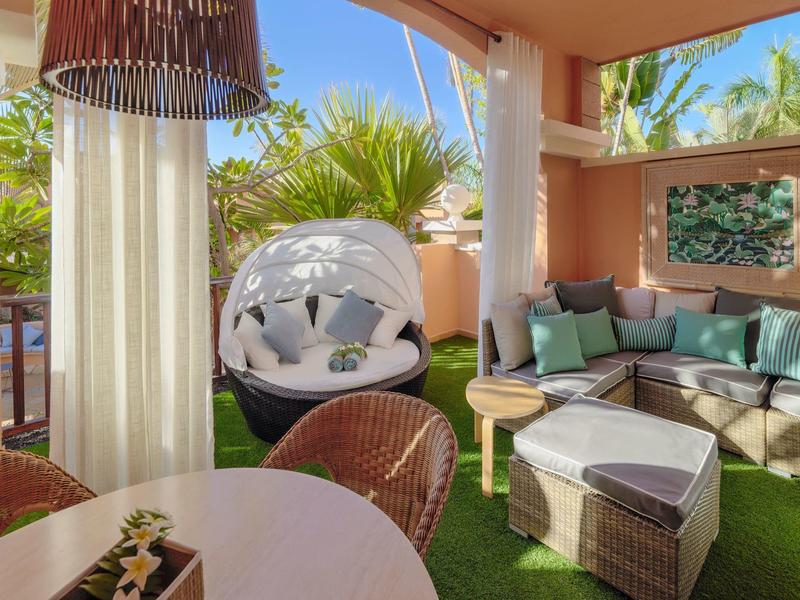 Gemütliche Terrasse mit gepolsterten Sitzmöbeln, Rundkorb-Sessel und Tisch, umgeben von grünen Pflanzen.