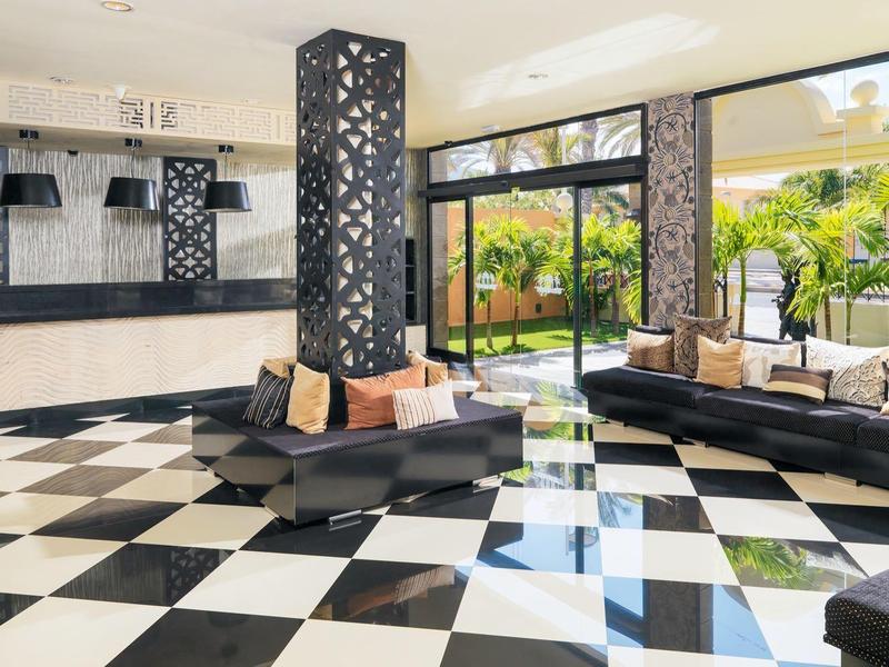 Großer Raum mit schwarz-weiß kariertem Boden, modernen Sitzgruppen und großen Fenstern zum Garten.