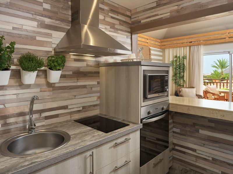 Moderne Küche mit Edelstahlspüle, Induktionskochfeld, eingebautem Backofen und Holzwandverkleidung.