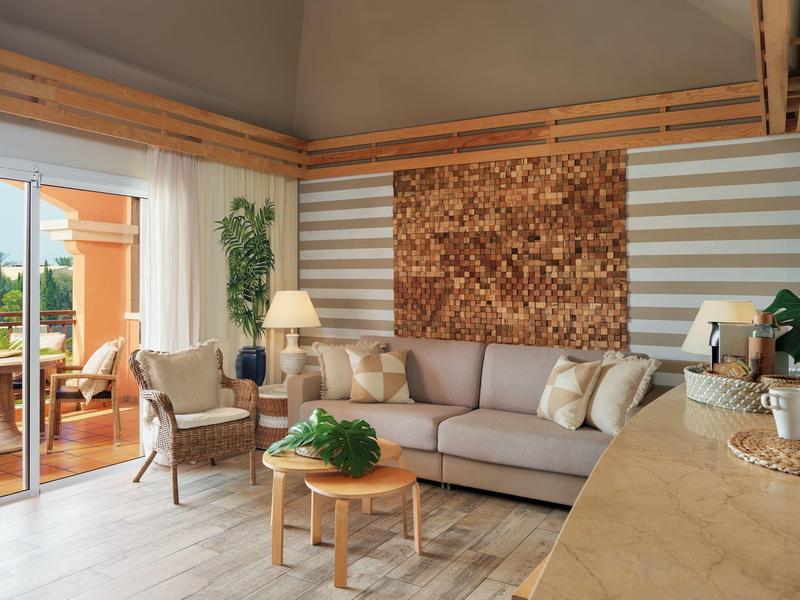 Helles Wohnzimmer mit grauem Sofa, Holztisch, Pflanzen und Zugang zur Terrasse mit Außenmöbeln.