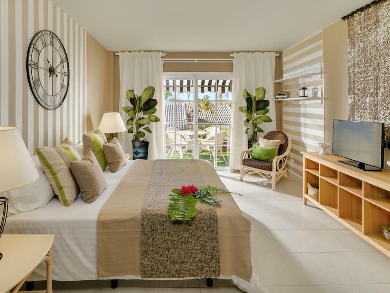 Helles Schlafzimmer mit Doppelbett, Pflanzen, Holzregal und großem Fenster mit Blick ins Grüne.