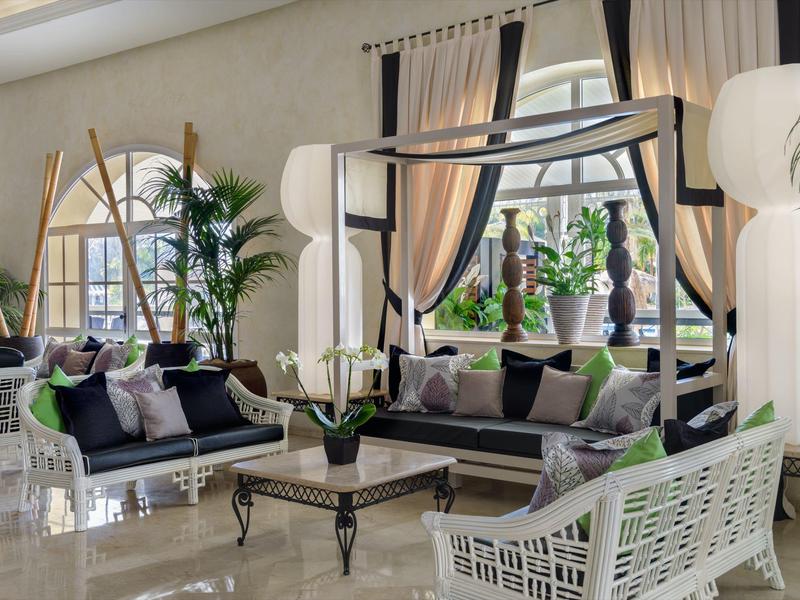 Elegantes Wohnzimmer mit großen Fenstern, weißen Wänden, schwarz-weißen Möbeln und vielen Pflanzen.