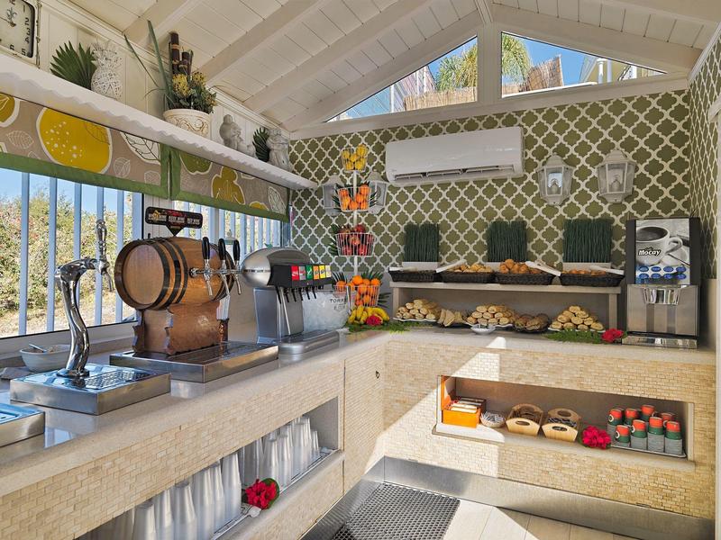 Moderne Bar mit Zapfhähnen, Fässern, Obstregal und heller, offener Raumgestaltung.