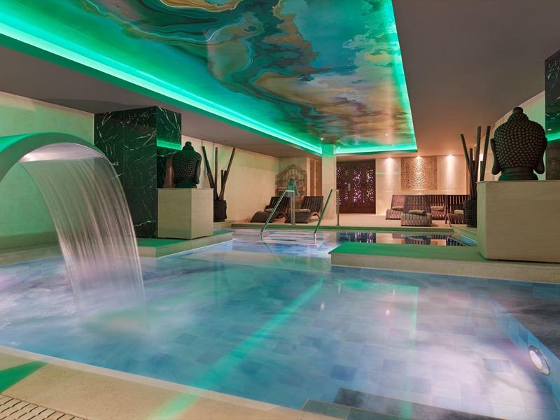 Moderner Innenpool mit Wasserfall, stimmungsvoller grüner Beleuchtung und gemütlichen Liegen.