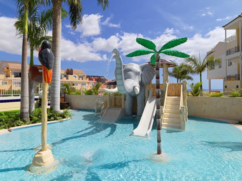 Wasserpark mit Elefant-Rutsche, Palmen und klarem blauen Wasser unter sonnigem Himmel.